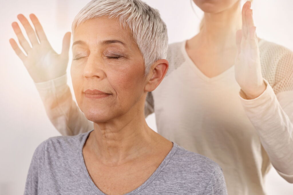Reiki Behandlung an Frau mit grauer Kurzhaarfrisur, Therapeutin steht hinter ihrem Rücken