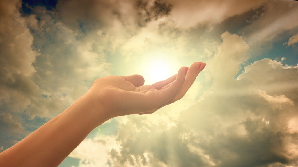 nach oben geöffnete Hand vor blauem Himmel mit weißen Wolken und Sonne