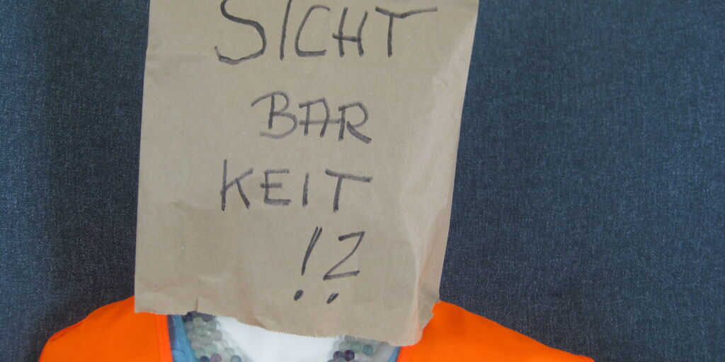 lebensgroße Puppe mit Warnweste; über den Kopf gezogen eine braune Papiertüte mit der Aufschrift 'Sichtbarkeit!?'