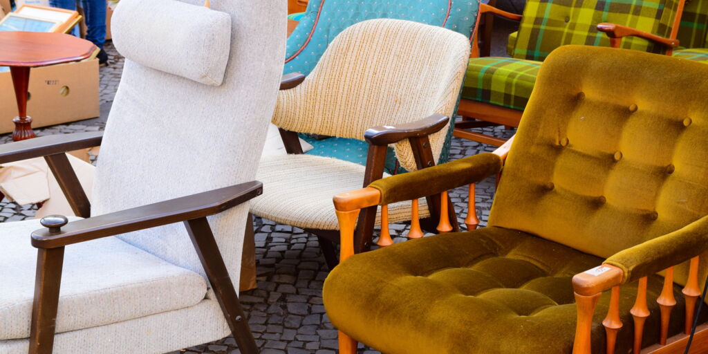 mehrere von Stil und Farbe unterschiedliche Sessel auf Flohmarkt auf Kopfsteinpflaster, alle nach links ausgerichtet