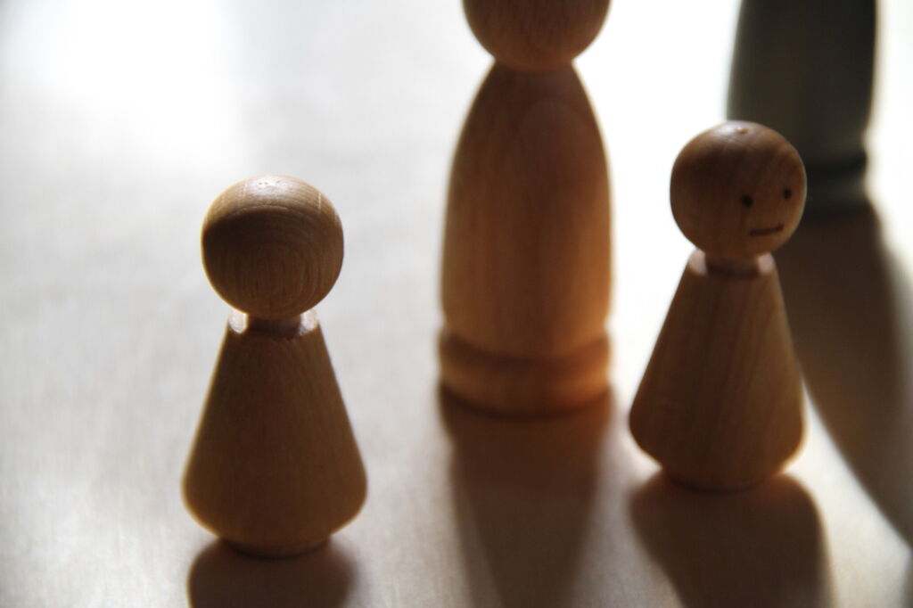 Familienbrett vier Holzfiguren stehen unterschiedlich nah beieinander, starkes Licht und Schatten Familienbrett vier Holzfiguren stehen unterschiedlich nah beieinander, starkes Licht und Schatten