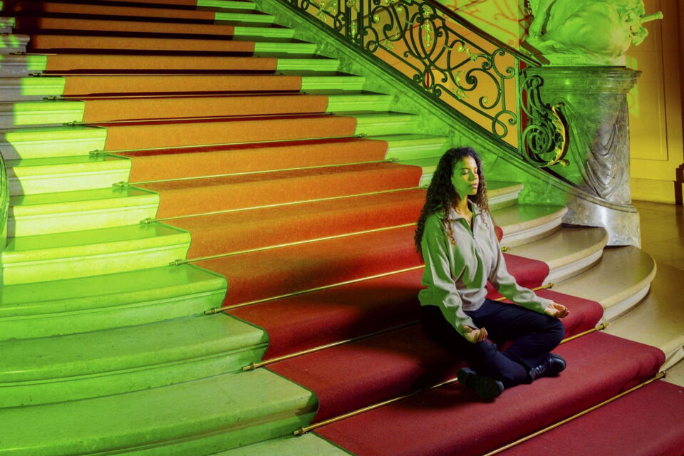 Meditierende Frau sitzt auf einer Treppe im lichtdurchfluteten Museum.