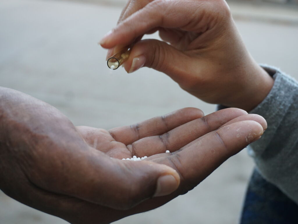 Eine Person gibt homöopathische Globuli aus einem Röhrchen in die offene Hand einer anderen Person.