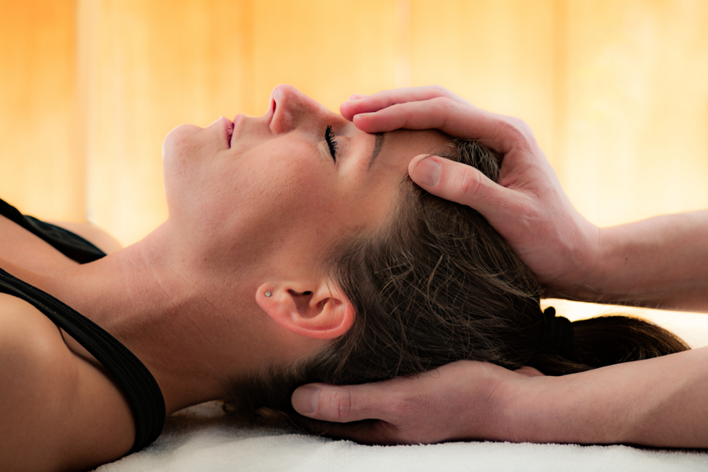 Craniosacrale Behandlung. Hände der Therapeutin halten von oben und unten den Kopf der auf dem Rücken liegenden Klientin
