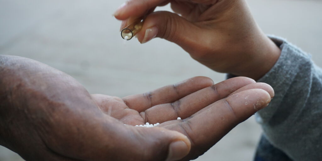Eine Person gibt homöopathische Globuli aus einem Röhrchen in die offene Hand einer anderen Person.