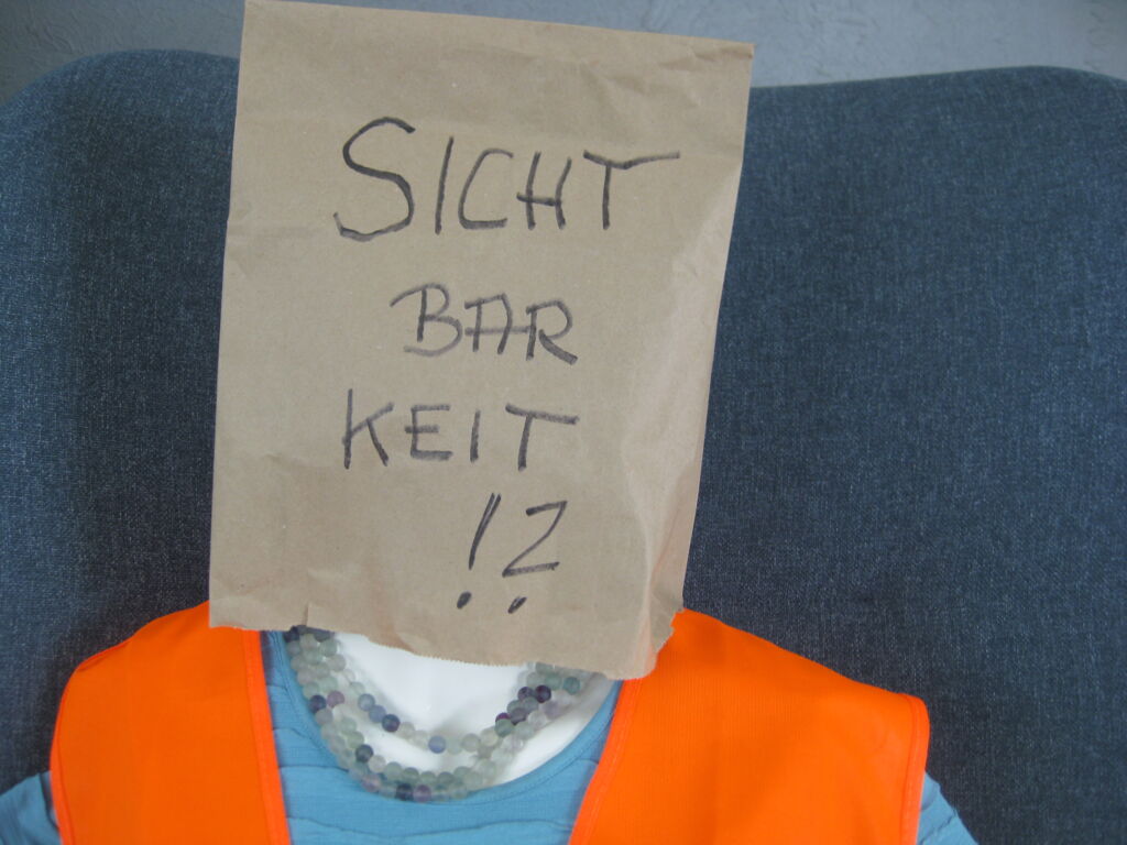 lebensgroße Puppe mit Warnweste; über den Kopf gezogen eine braune Papiertüte mit der Aufschrift 'Sichtbarkeit!?'