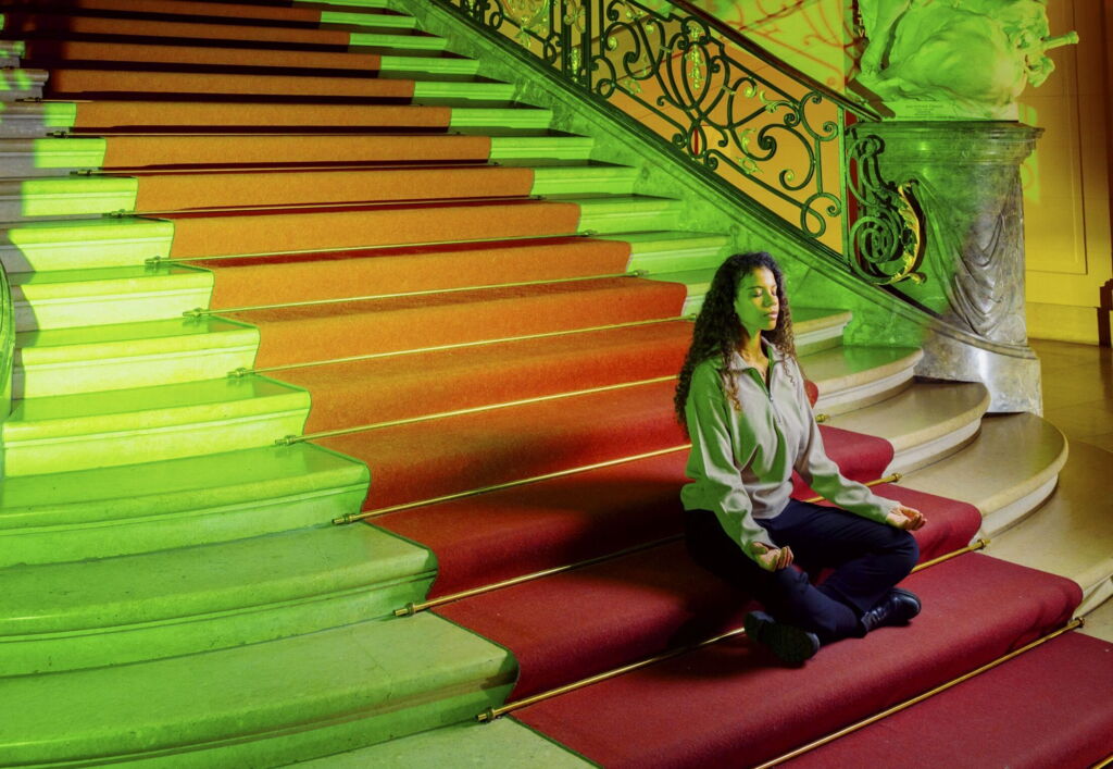 Meditierende Frau sitzt auf einer Treppe im lichtdurchfluteten Museum.